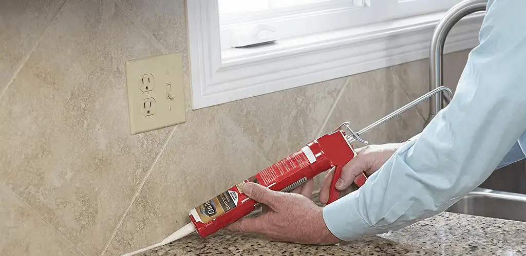 Handyman applying caulk along a kitchen backsplash and countertop seam in Sioux Falls, SD