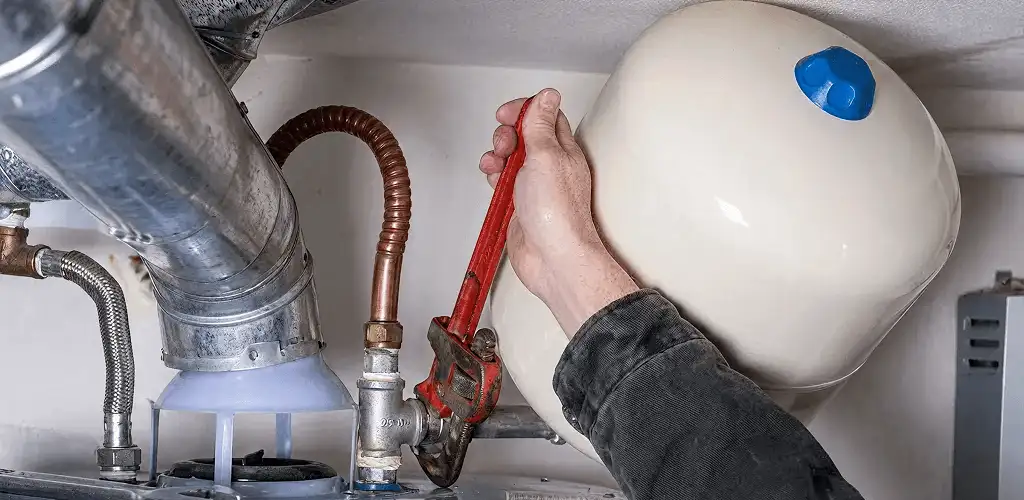 Water heater repair technician tightening plumbing connections near a tank unit in Sioux Falls, SD